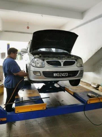 Silver car on a lift with its hood open inside a service workshop