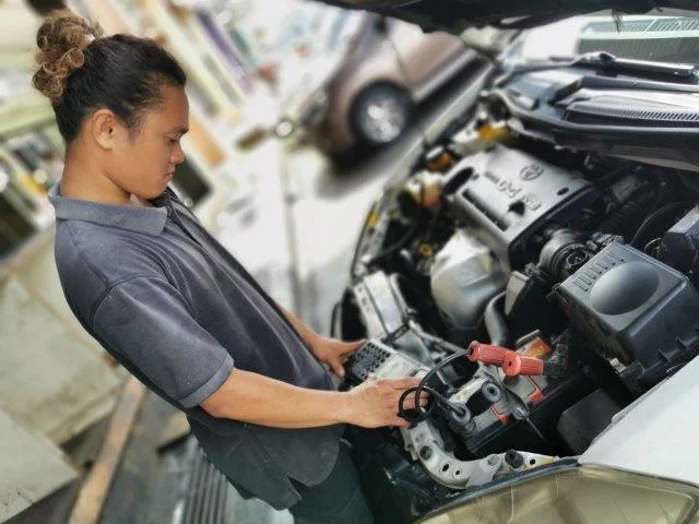 Technician using a handheld tester at the open engine bay of a vehicle