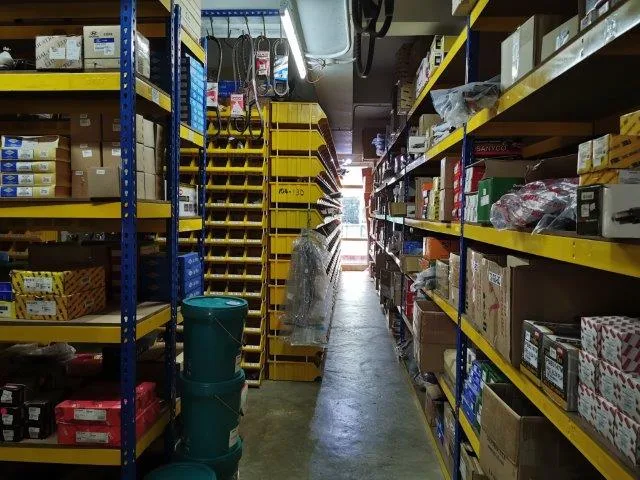 Narrow aisle between yellow industrial racks stacked with cartons and plastic bins